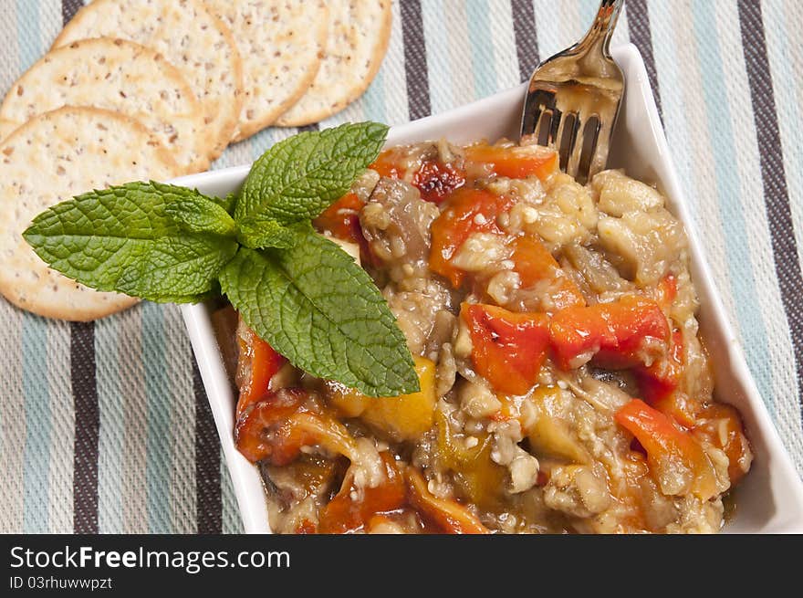 Colorfull roasted vegetables salad with round crackers on a table