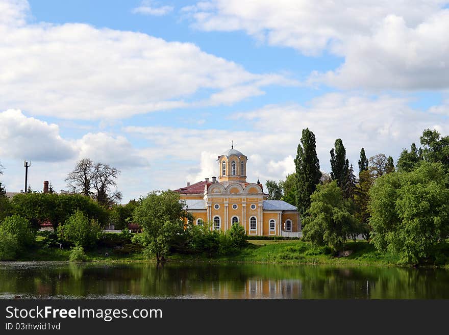 Church on the riverbank with a blue sky and green trees.