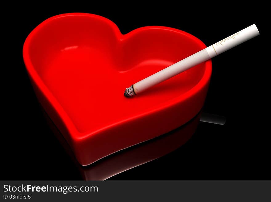 Red ashtray with a cigarette on a black background