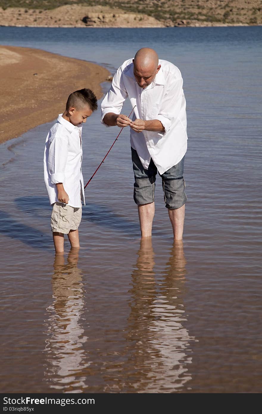 A father fixing his sons pole so he can fish. A father fixing his sons pole so he can fish.