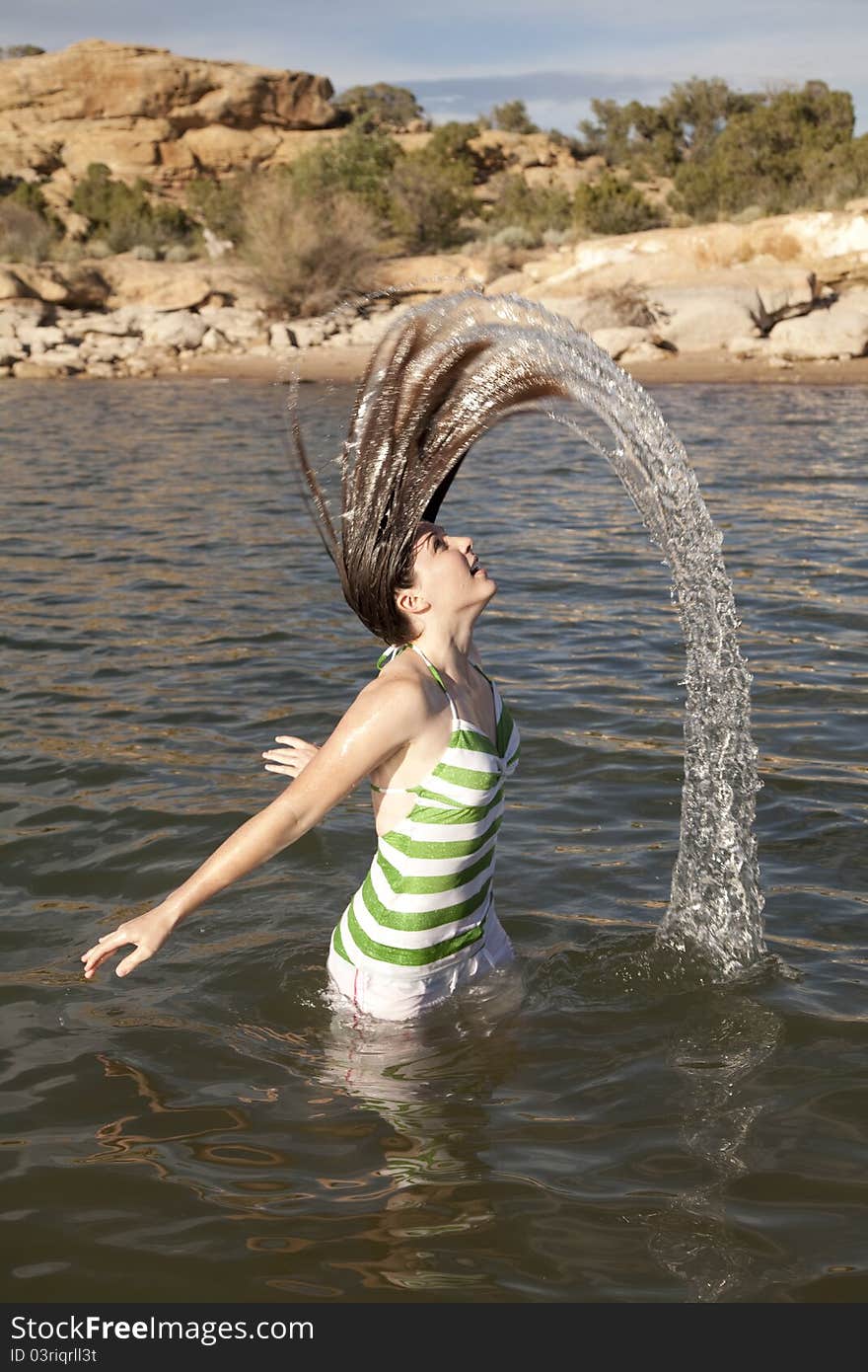 A woman standing waist deep in the water fliping her hair to make a water rainbow. A woman standing waist deep in the water fliping her hair to make a water rainbow.