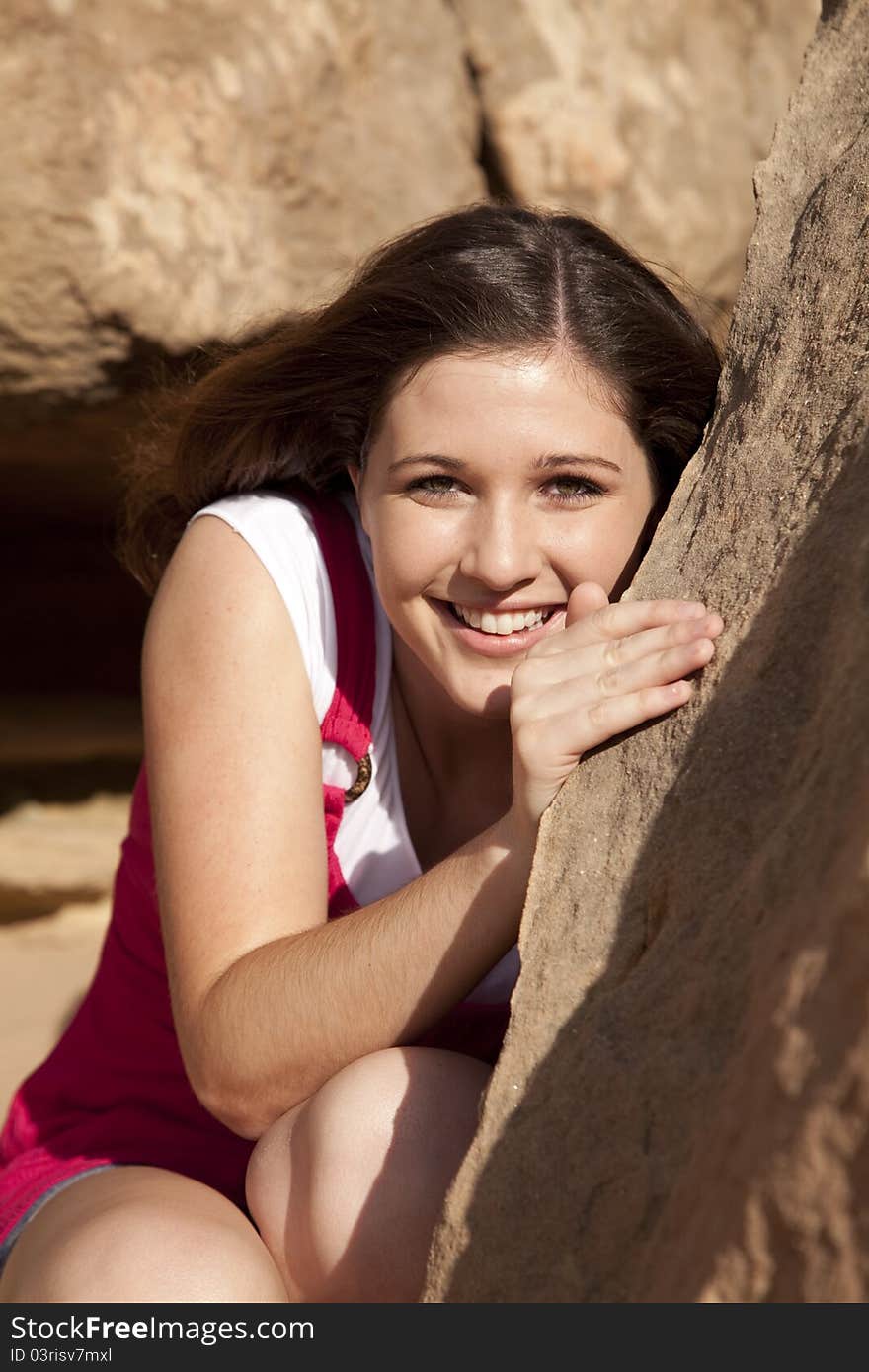 A beautiful woman hiding behind a rock in the outdoors with a smile on her face. A beautiful woman hiding behind a rock in the outdoors with a smile on her face.