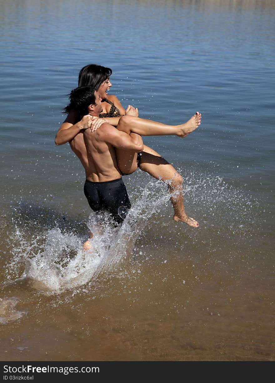 A men carrying his girlfriend out to the water kicking and screaming. A men carrying his girlfriend out to the water kicking and screaming.