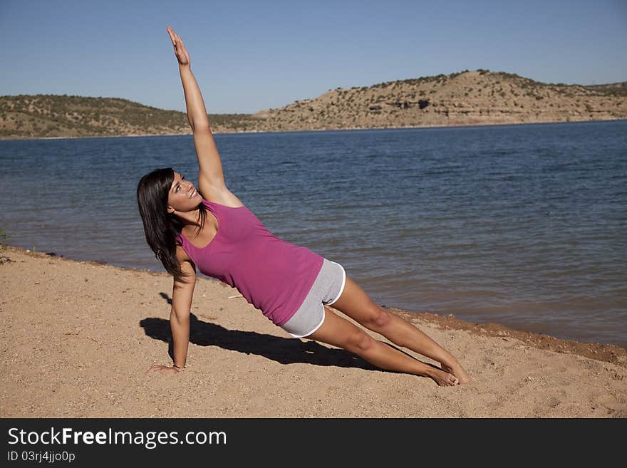 A woman doing her yoga stretch on the beach with a smile on her face.