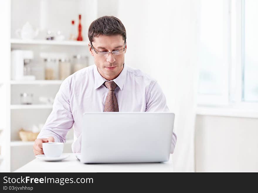 A man with a laptop and a cup in the kitchen. A man with a laptop and a cup in the kitchen