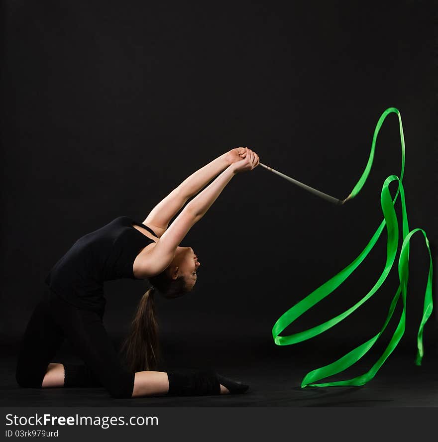 Attractive woman dancing with green ribbon against dark background. Attractive woman dancing with green ribbon against dark background