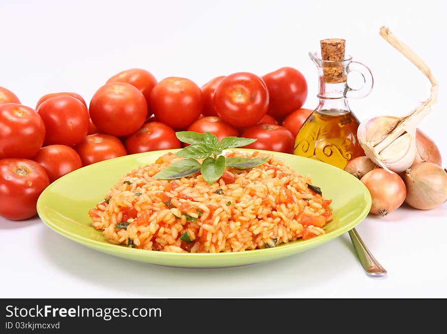 Risotto with tomatoes on a green plate decorated with basil with fresh tomatoes, onions, garlic and olive oil on white background