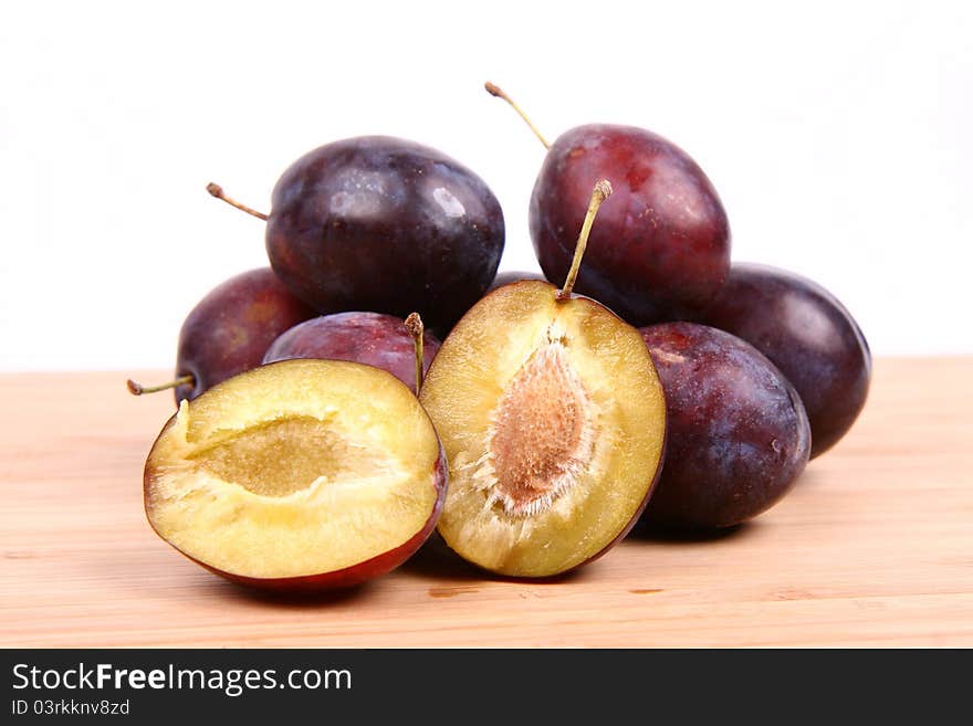 Plums on white background - one cut in half with a pit visible