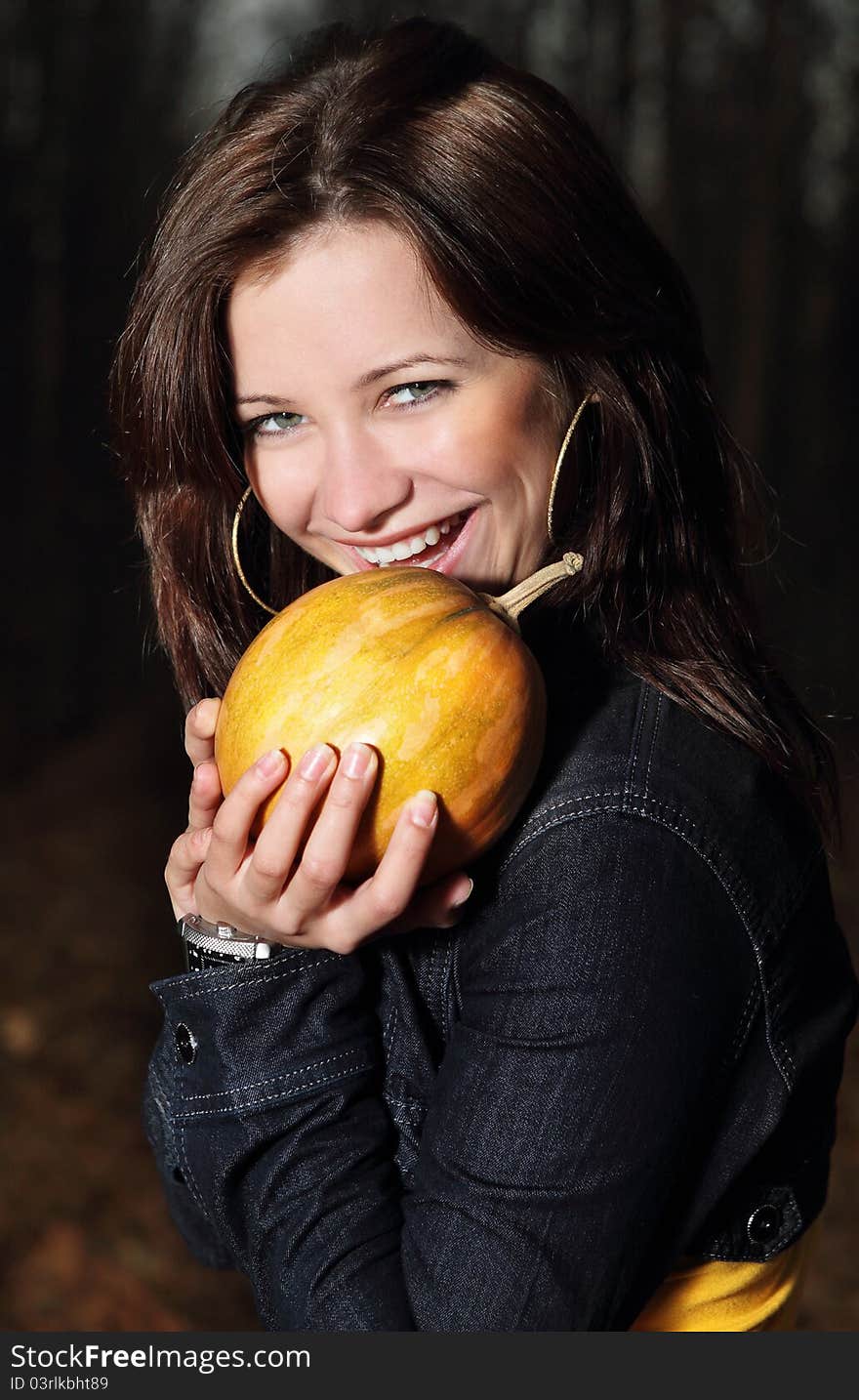 Smiling brunette girl with pumpkin in dark forest. Smiling brunette girl with pumpkin in dark forest