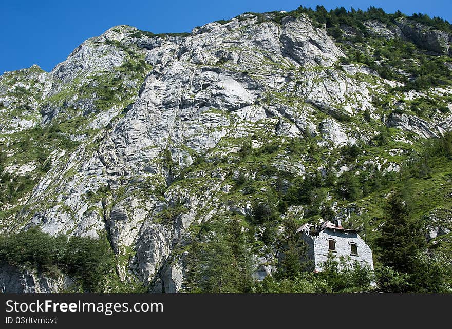 An old, ruined house in front of a huge rock wall. An old, ruined house in front of a huge rock wall