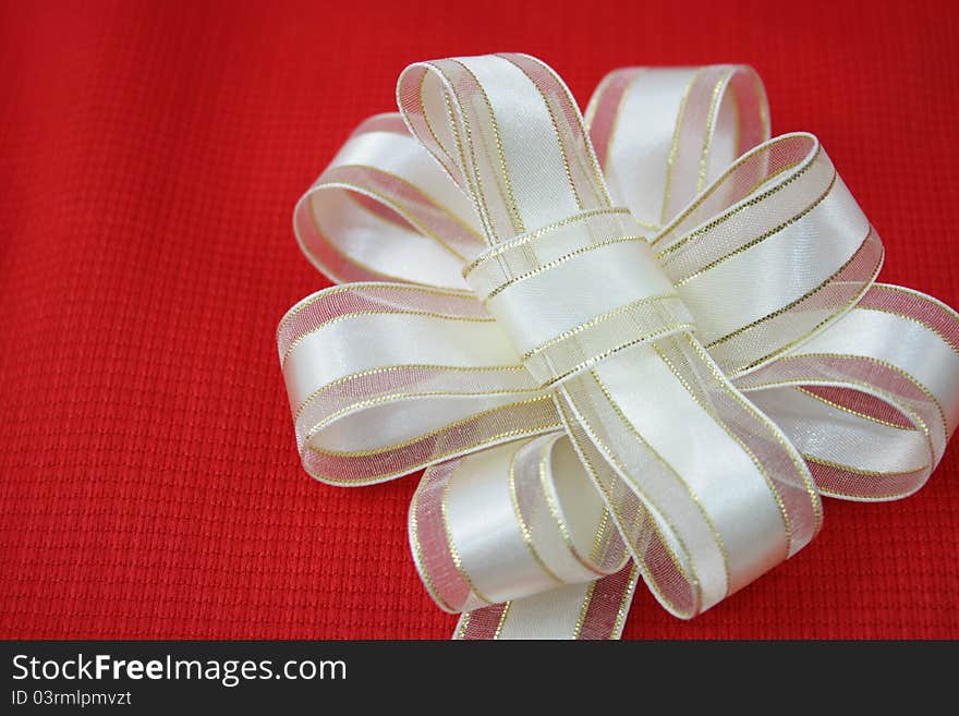 Cream and gold ribbon flower on red background.