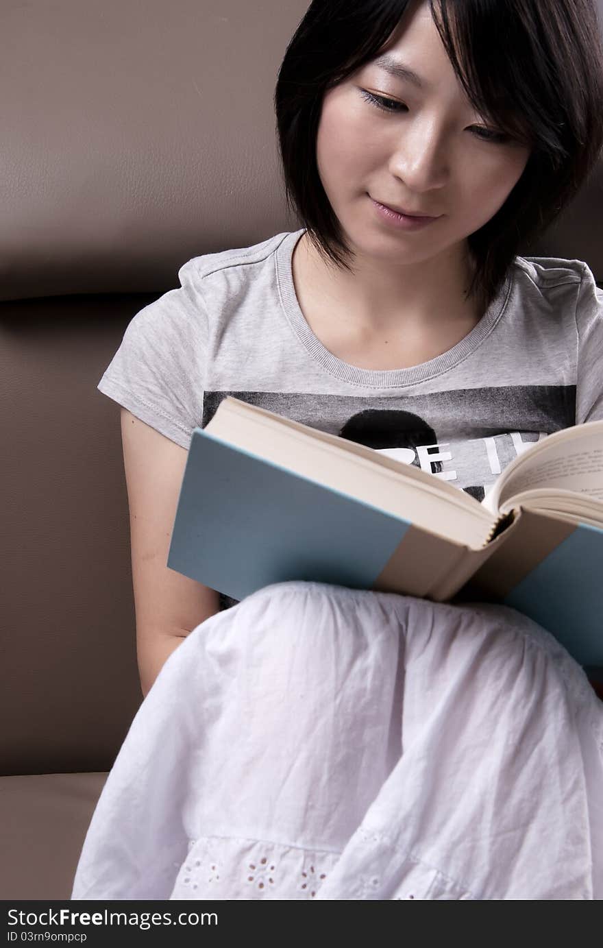 Young woman sitting on sofa reading book