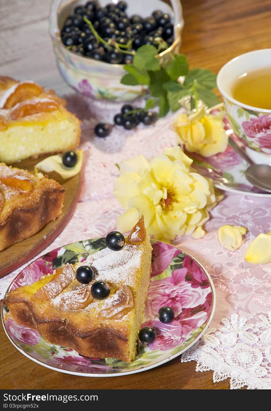 Cheese cake with apricots and a cup of green tea on a little table decorated with petals of roses. Cheese cake with apricots and a cup of green tea on a little table decorated with petals of roses