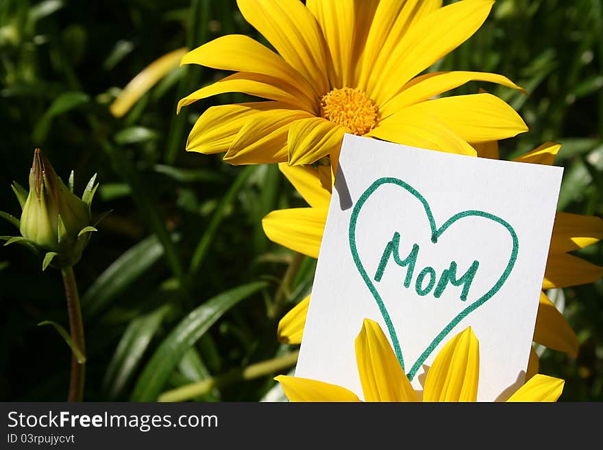 Flowers with a heart with the word Mom in it on a white paper sign. Flowers with a heart with the word Mom in it on a white paper sign.