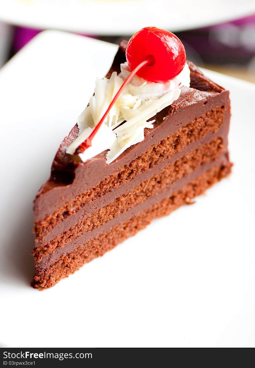 A soft chocolate cake with cherry on white dish