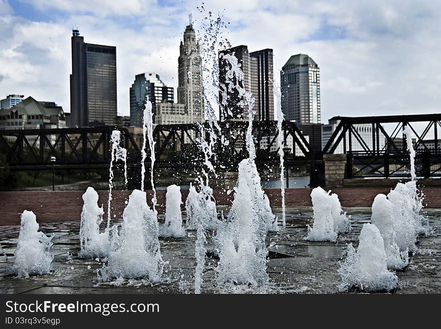 A photo of a fountain with a city scape in the background. A photo of a fountain with a city scape in the background.