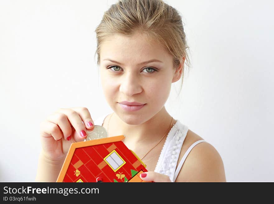 teenage girl putting a big silver coin in her moneybox looking at the camera. teenage girl putting a big silver coin in her moneybox looking at the camera