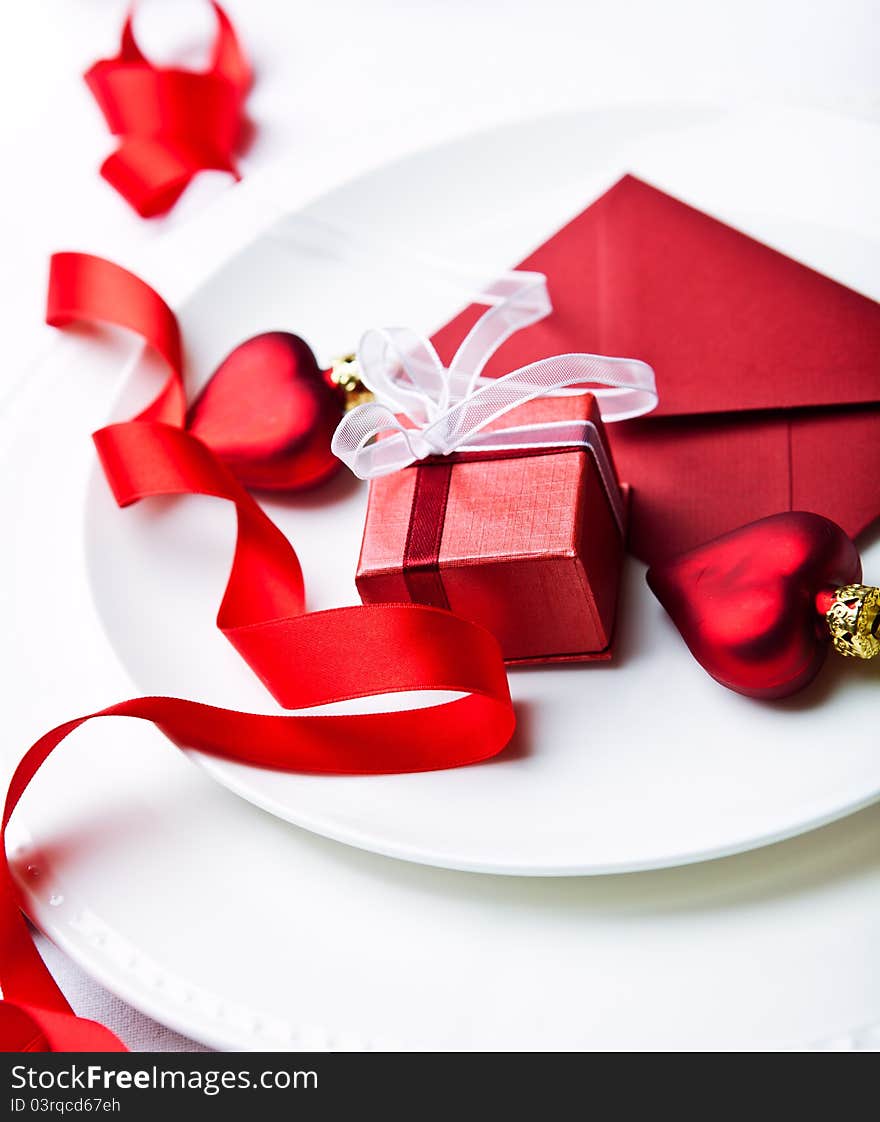 Close up of a little red gift box, envelope and christmas ornaments on white plates. Close up of a little red gift box, envelope and christmas ornaments on white plates