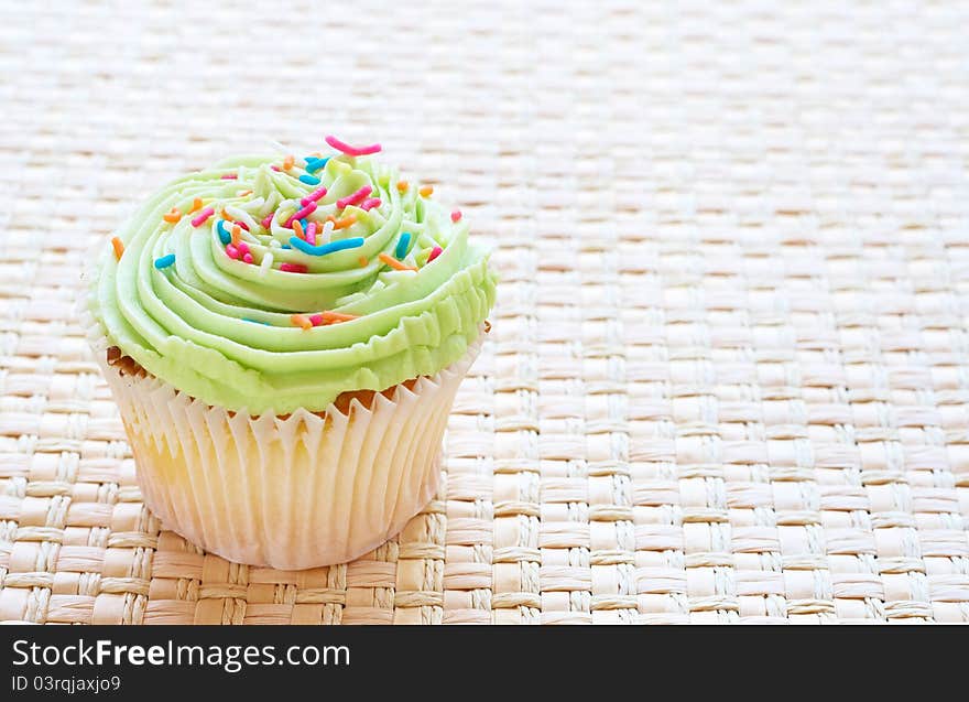 Fresh vanilla cupcake with lime icing on woven straw background