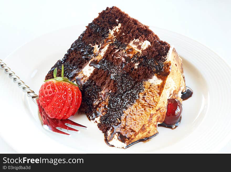 Slice of Black Forest cake with fresh cream and cherries, served on a white plate with silver fork