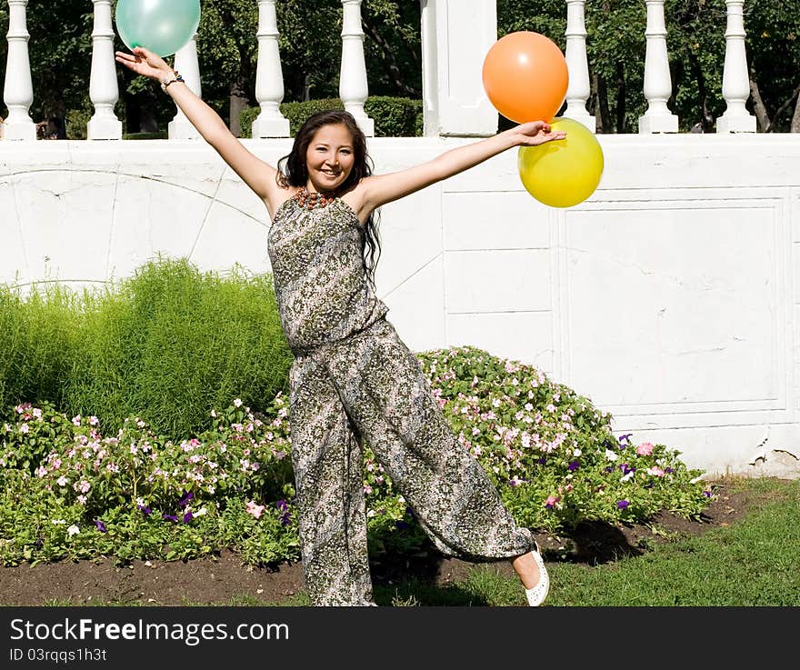 Joyful pregnant girl with colorful balloons walking in park