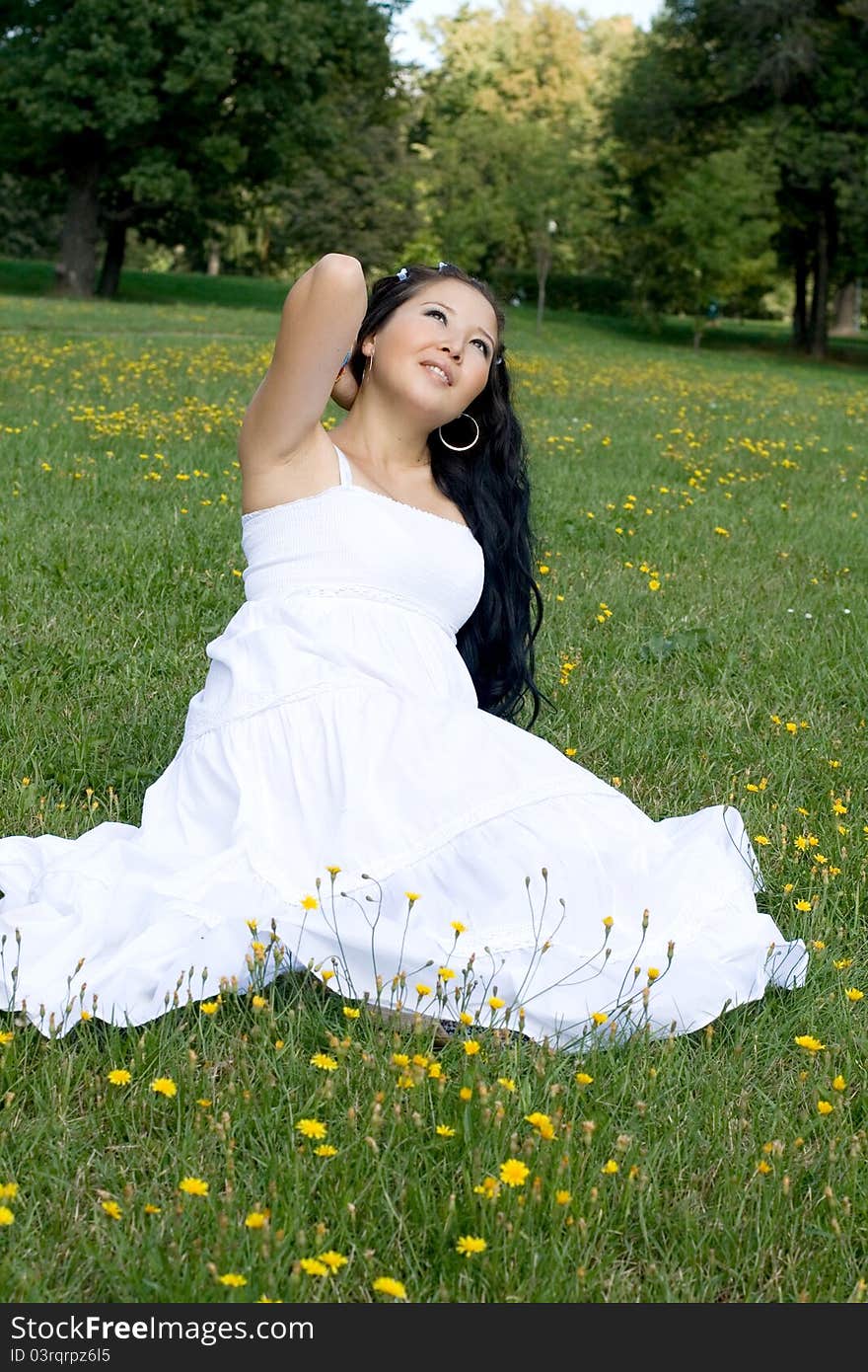 Beautiful pregnant girl sitting on grass among flowers