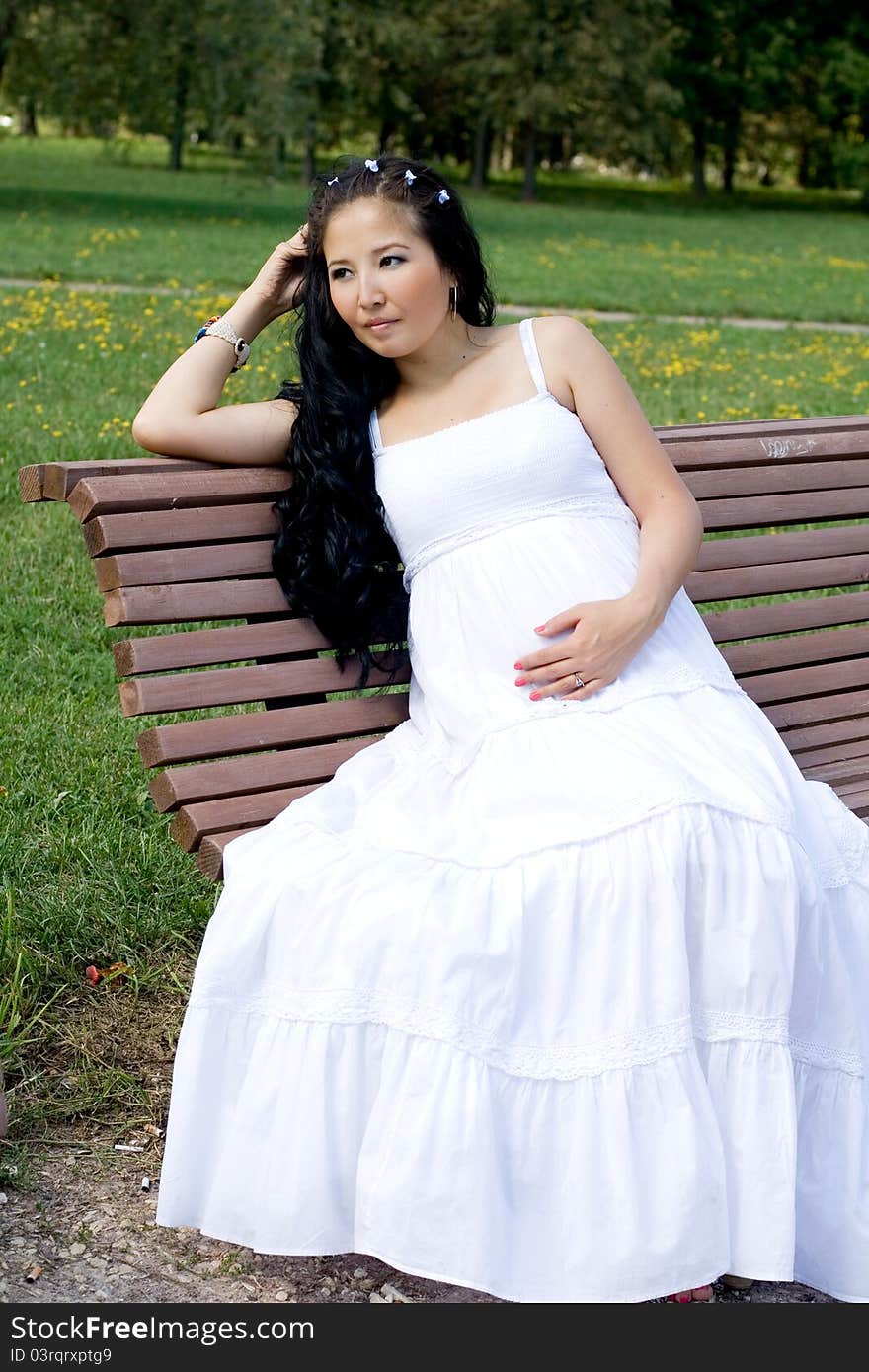 Beautiful pregnant girl sitting on bench in park