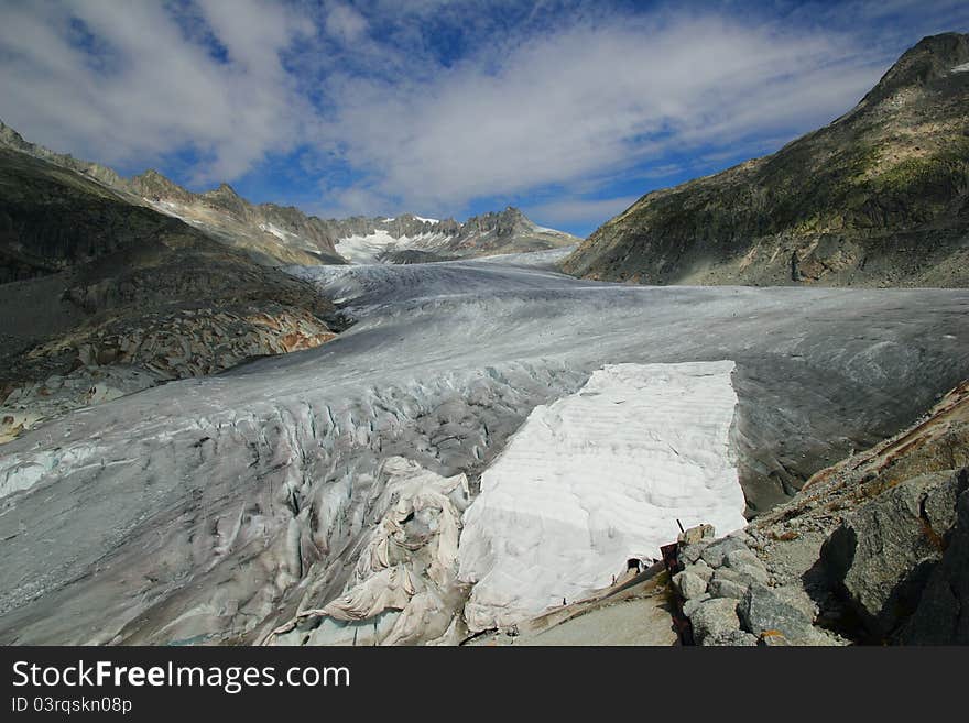 View on the Rhone glacier, covered with dirt. Entrance to the ice cave carved in it is covered with fleece to prevent melting. Glacier is receding rapidly due to the global warming. View on the Rhone glacier, covered with dirt. Entrance to the ice cave carved in it is covered with fleece to prevent melting. Glacier is receding rapidly due to the global warming.