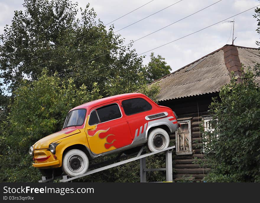 Funny picture, flashes of flame on the sides of the machine, ridiculous object against the background of a fun house, horizontal. Funny picture, flashes of flame on the sides of the machine, ridiculous object against the background of a fun house, horizontal