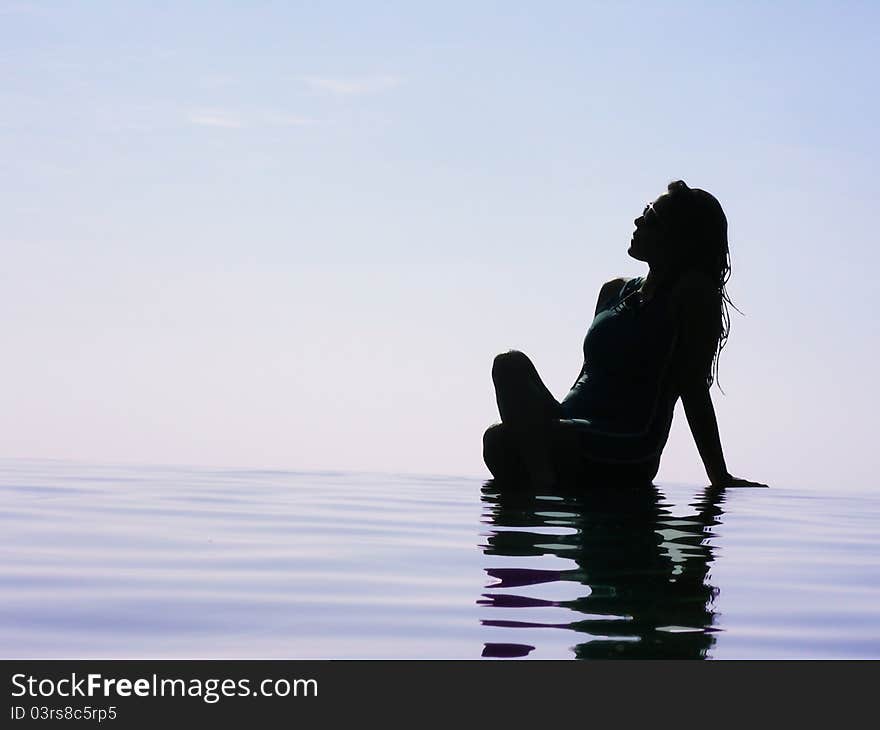 A silhouette of a woman basking in the Sun at the pool, during the early hours.