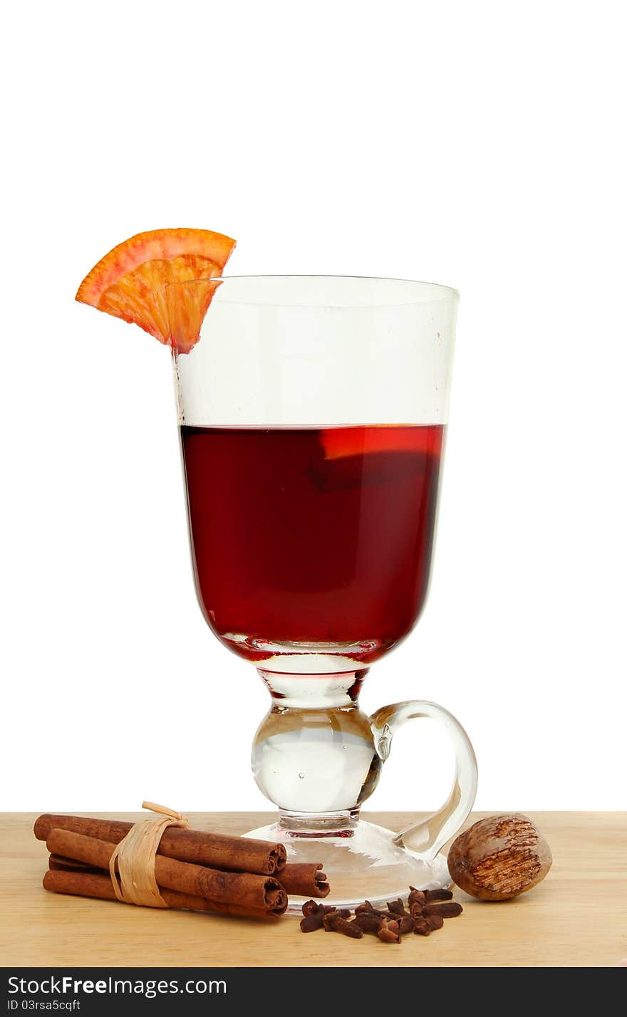 Glass of mulled wine with a slice of orange and spices on a wooden surface against a white background