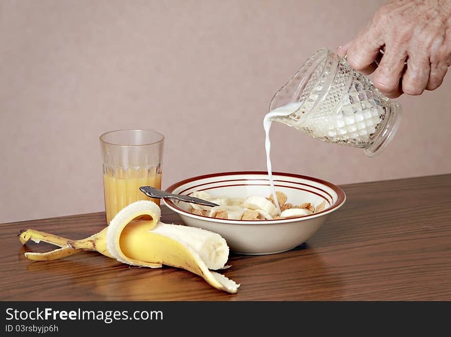 Male hand pouring milk into breakfast cereal. Orange juice and banana on table.