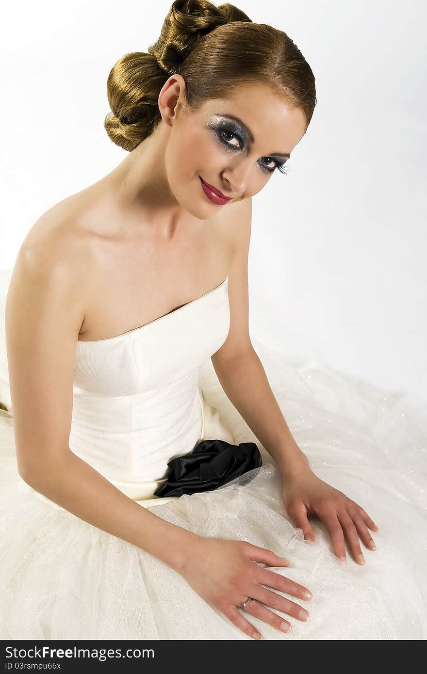 Beautiful young bride with extremly long hair, and nice make up, with long eyelashes in a white wedding dress before a white background looking up and sitting. Beautiful young bride with extremly long hair, and nice make up, with long eyelashes in a white wedding dress before a white background looking up and sitting