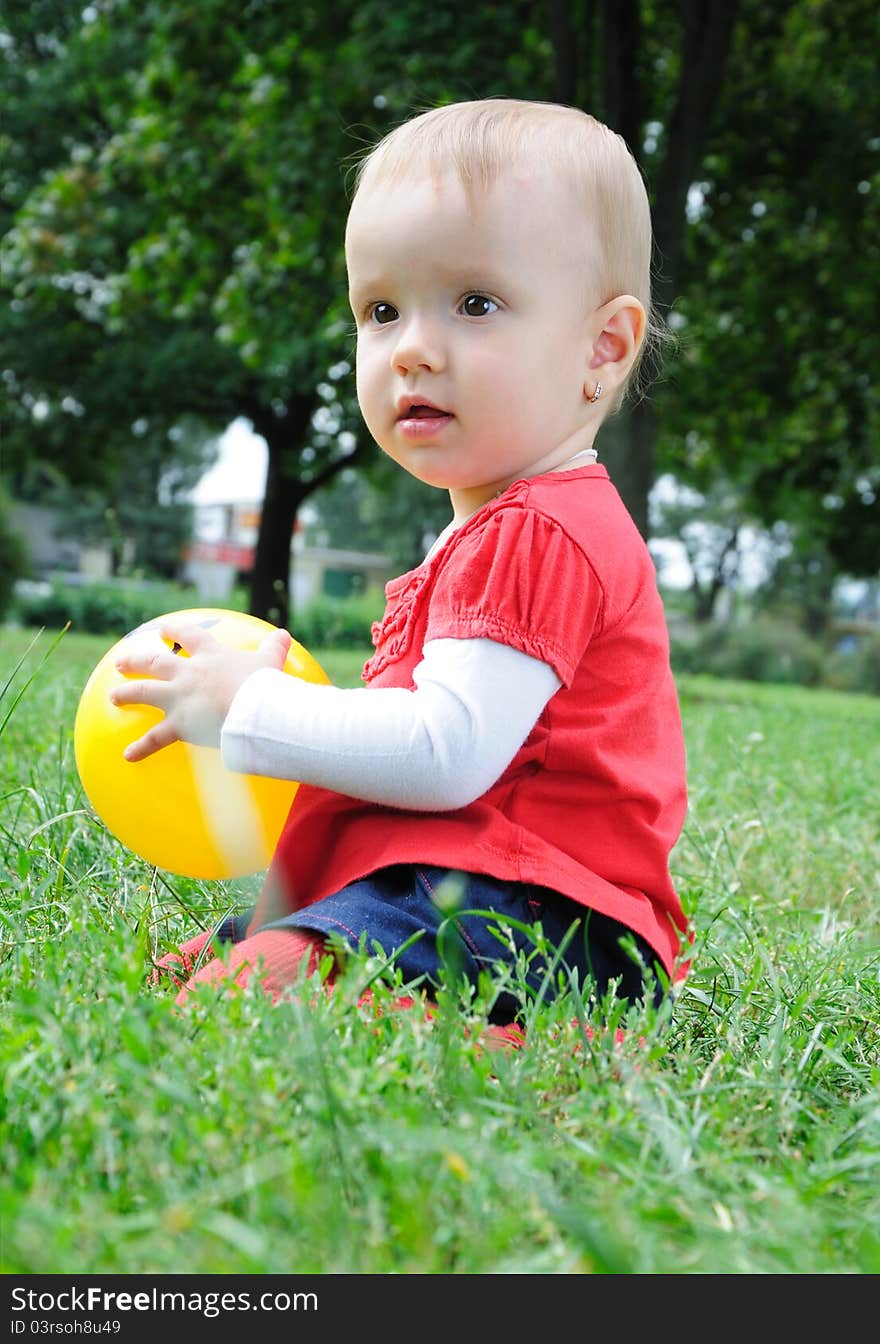 Cute little girl playing with yellow ball on the meadow