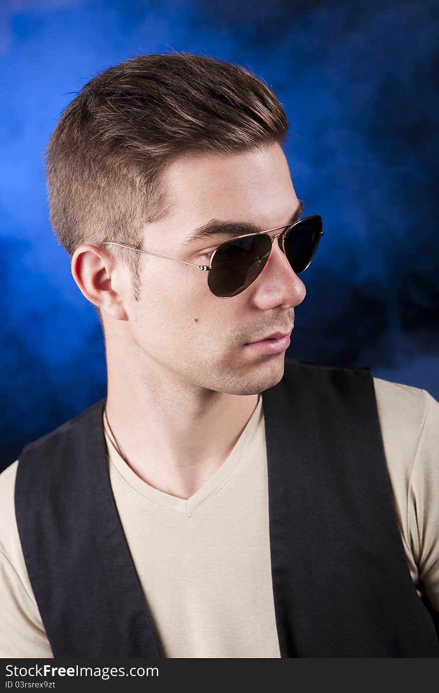 Handsome young male model with aviator sunglasses before a blue smoke background. Handsome young male model with aviator sunglasses before a blue smoke background.