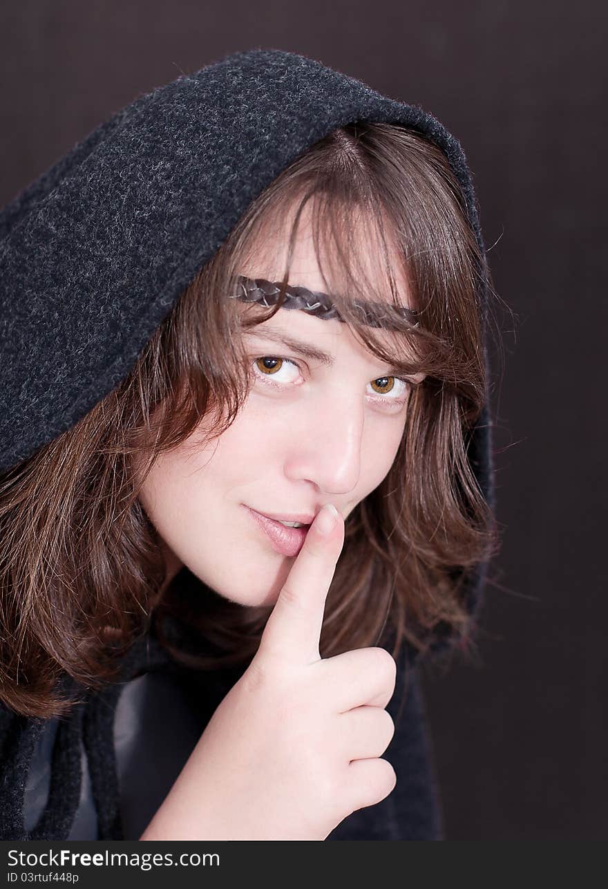 Woman in black hood puts forefinger to lips as a sign of silence on white background. Woman in black hood puts forefinger to lips as a sign of silence on white background