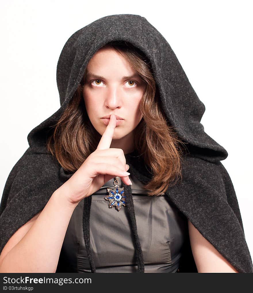 Woman in black hood puts forefinger to lips as a sign of silence on white background. Woman in black hood puts forefinger to lips as a sign of silence on white background