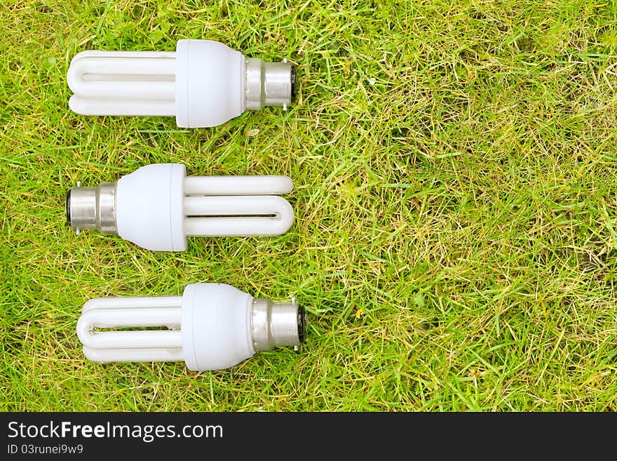 Three energy saving light bulks arranged in a pattern on some grass. Symbolising green energy. Three energy saving light bulks arranged in a pattern on some grass. Symbolising green energy.