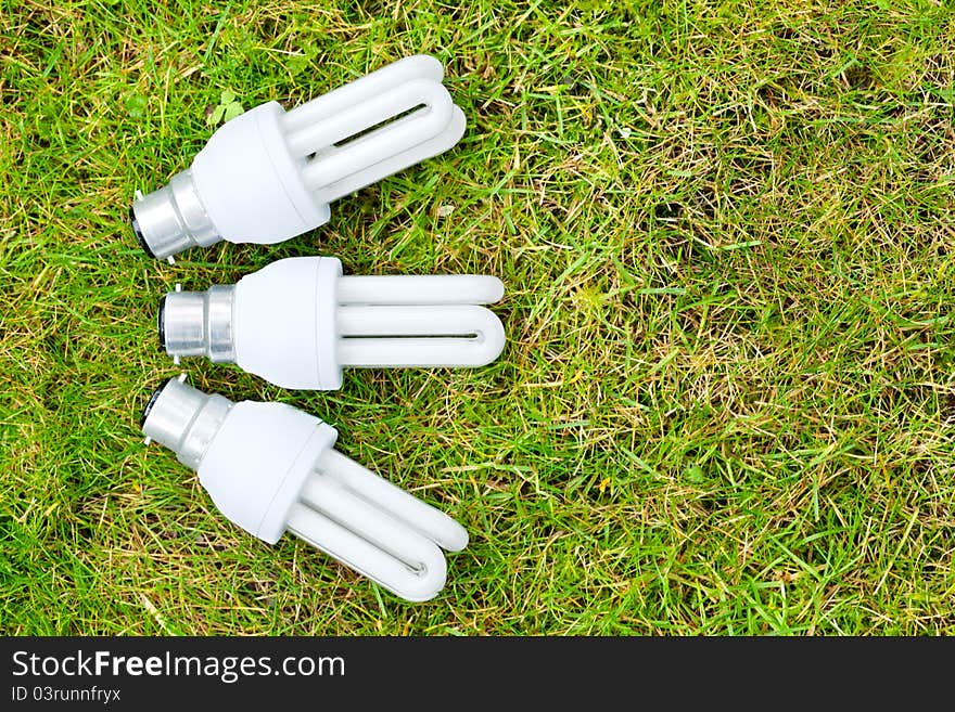 Three energy saving light bulks arranged in a fan pattern on some grass. Symbolising green energy. Three energy saving light bulks arranged in a fan pattern on some grass. Symbolising green energy.