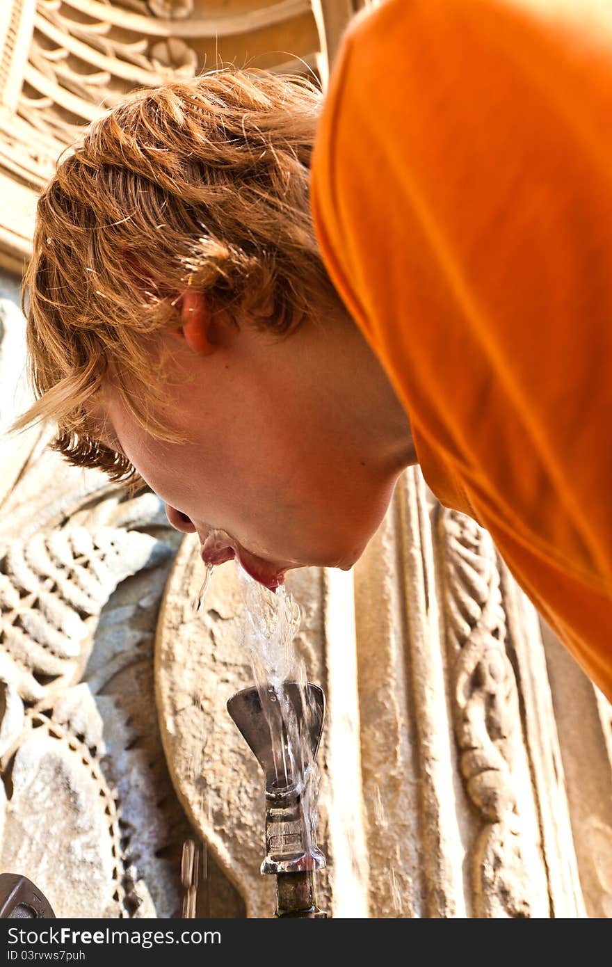 Boy is drinking water on a public fountain