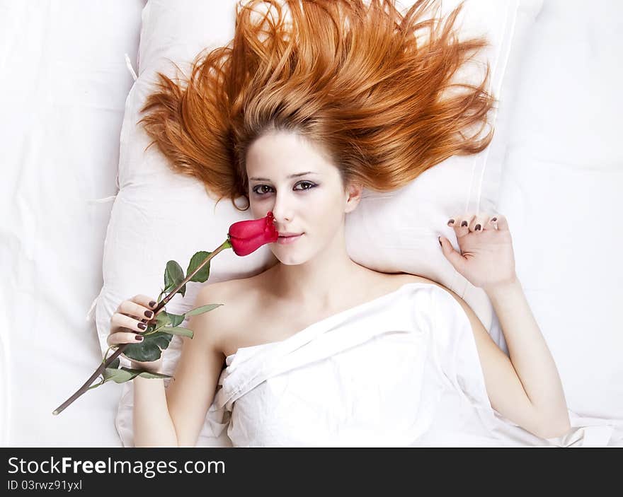 Fashion red-haired girl with rose in the bedroom. Studio shot from top.