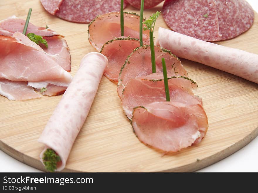 Ham with salami and herbs on wooden plate