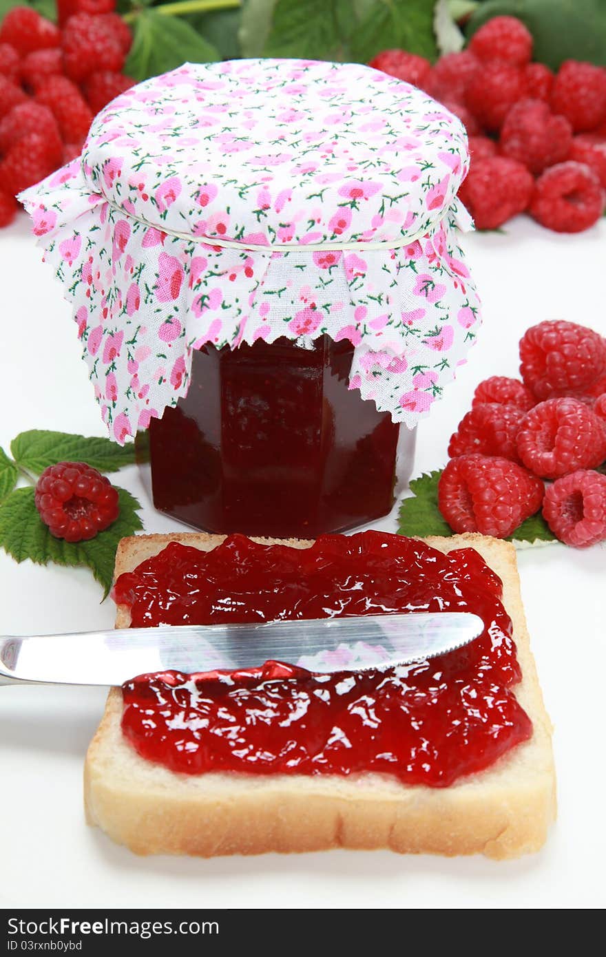 A glass of homemade raspberry jam with a toast, fresh fruits and leaves