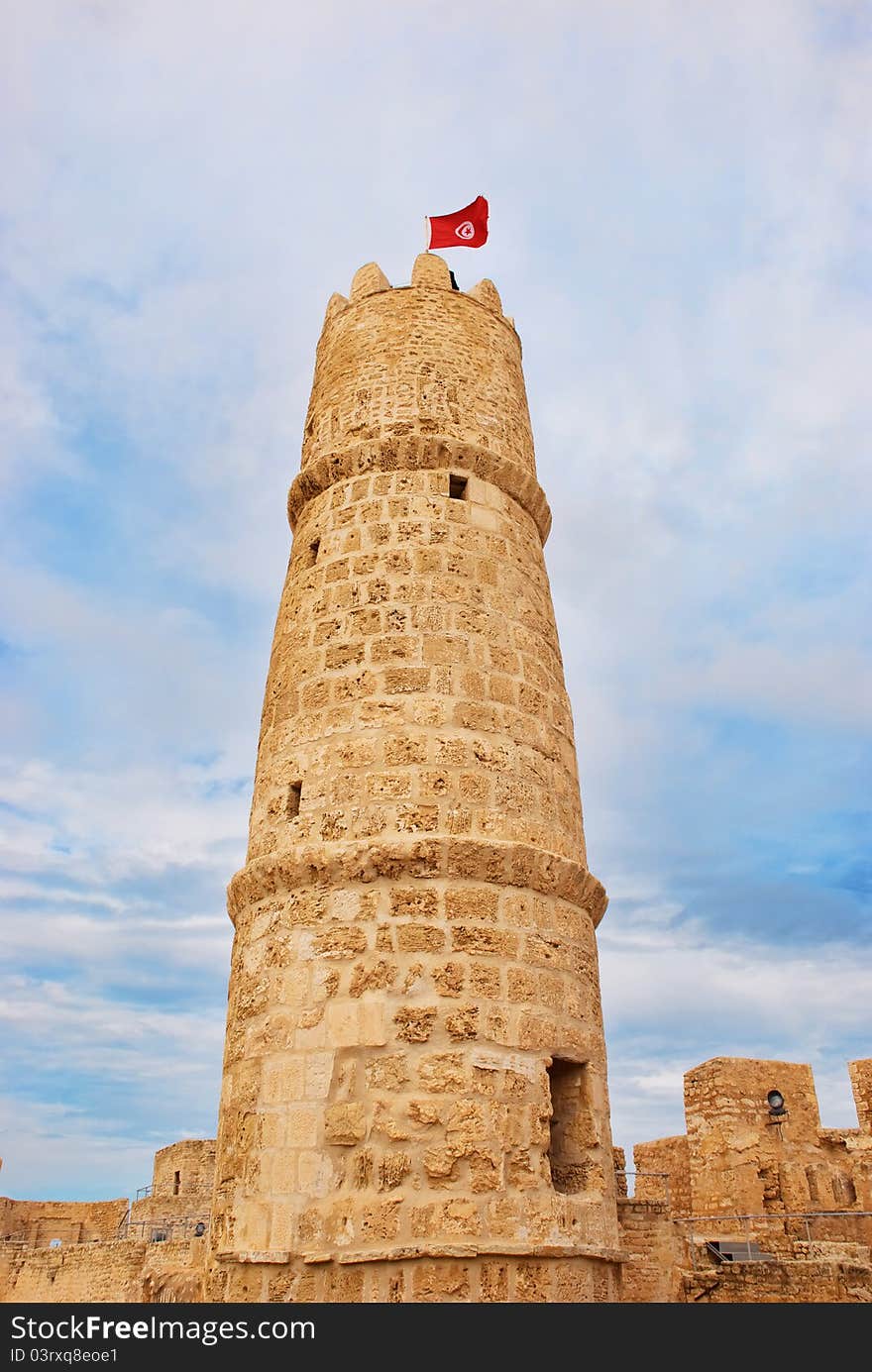 Tower of ribat in Monastir, Tunisia with tunisian flag against cloudy sky. Tower of ribat in Monastir, Tunisia with tunisian flag against cloudy sky