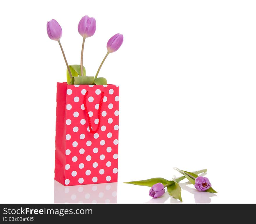 Three purple tulips in a little shopping bag isolated over white background