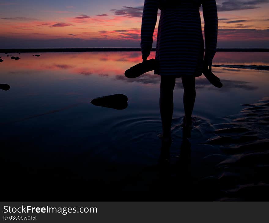 Silhouette of a child standing in a beach pool with beautiful sunset.