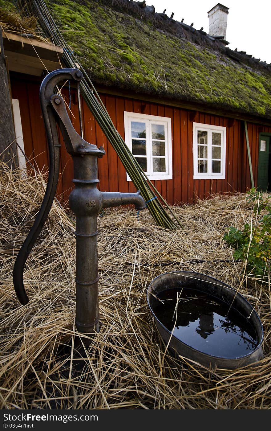 An old water pump on a farm with a red cottage in the background