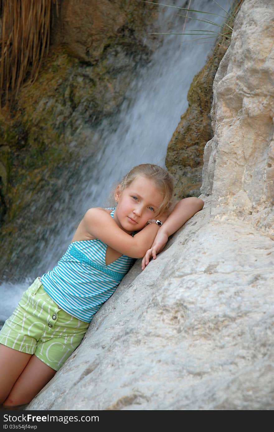 Child girl on the background of a waterfall poses