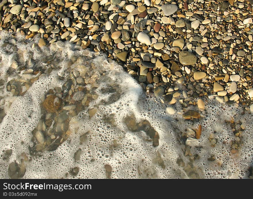 Sea waves lapping on the pebbles in the rays of the rising summer sun. Sea waves lapping on the pebbles in the rays of the rising summer sun