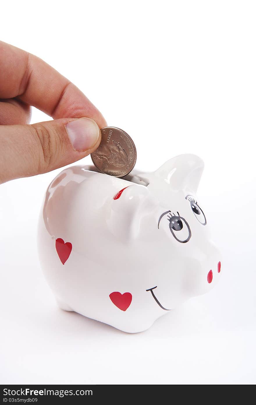 Hand inserting a coin in a piggy bank against a white background. Hand inserting a coin in a piggy bank against a white background